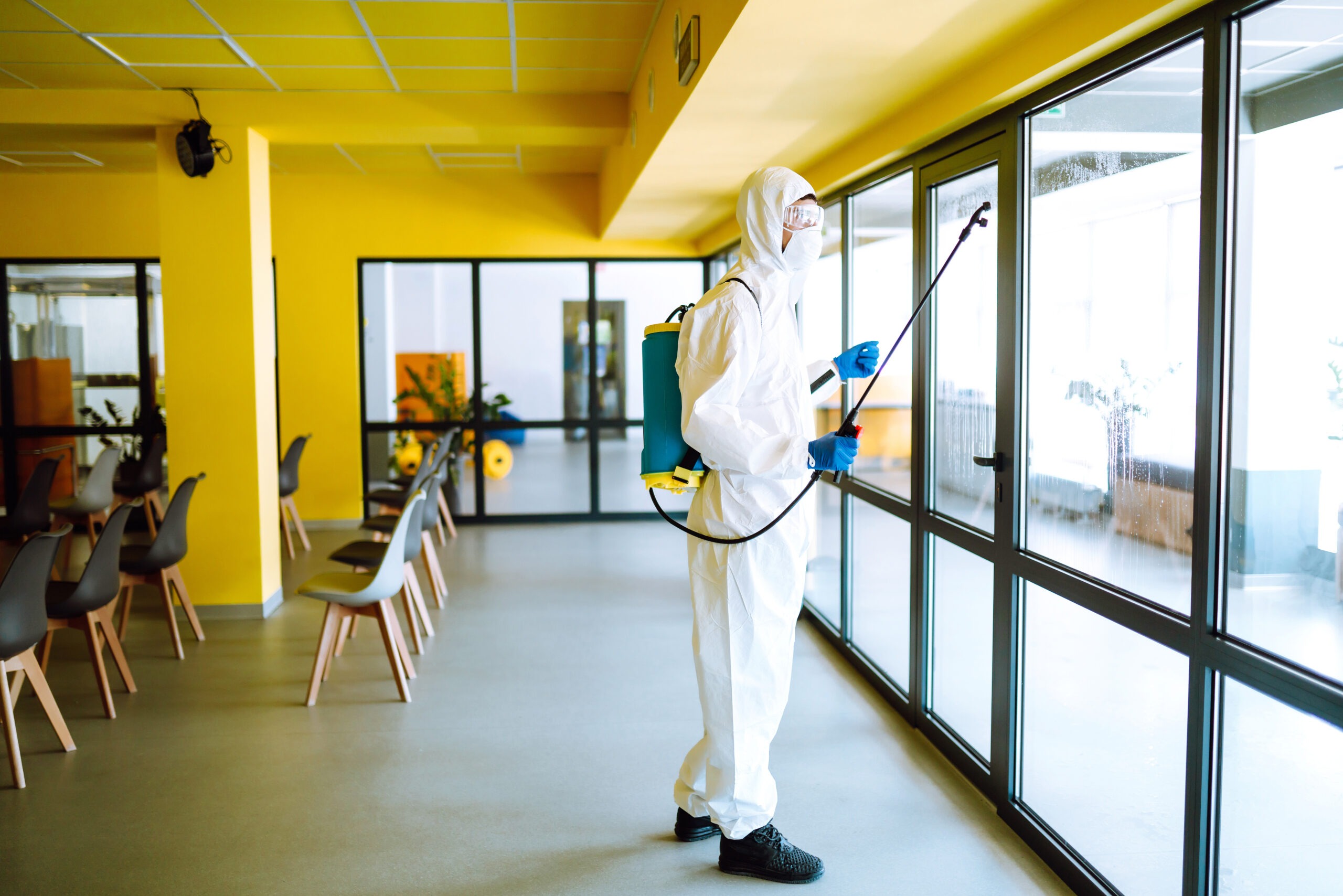 Disinfection Specialist in Protective Gear Spraying Disinfectant on Glass Doors